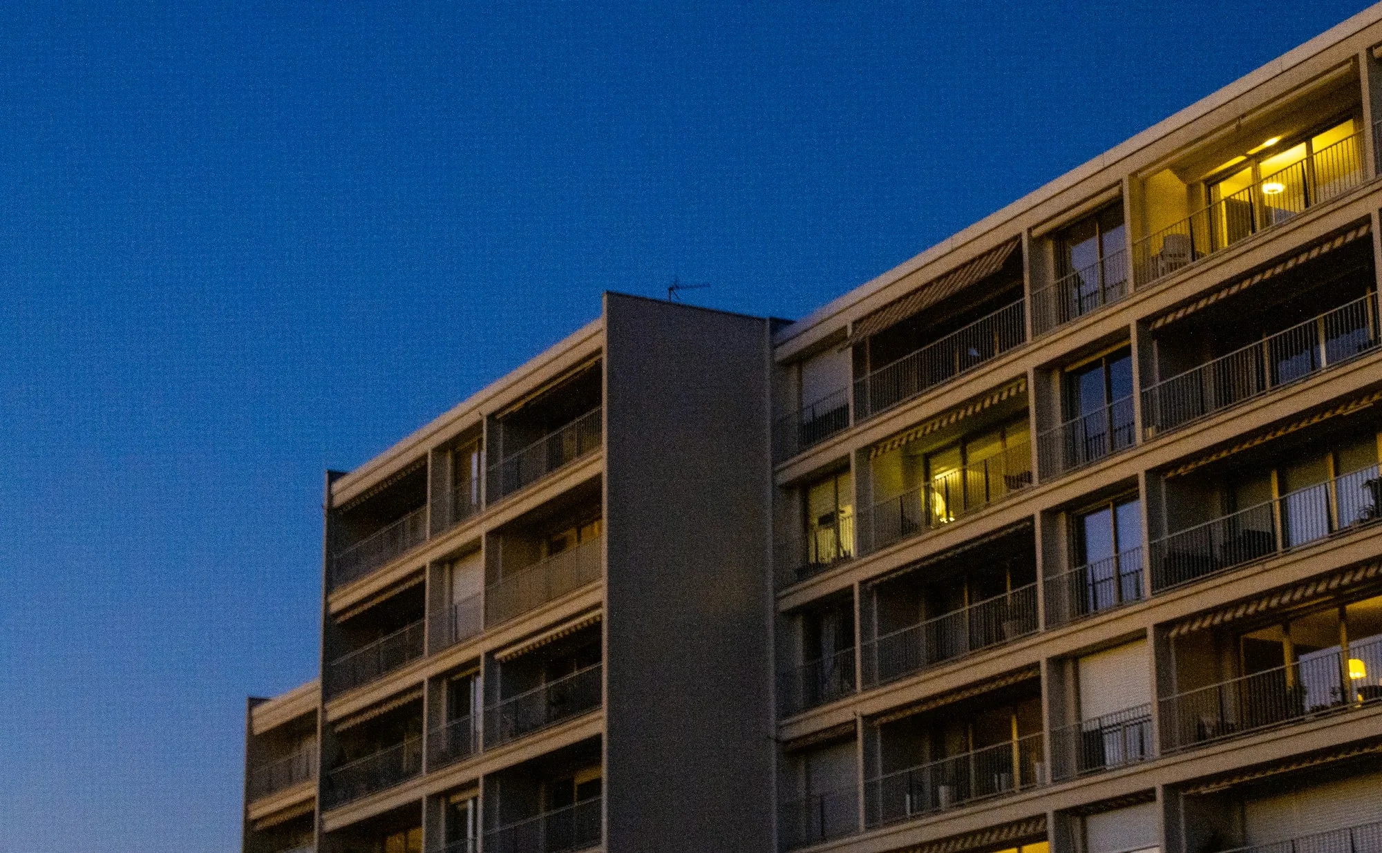 Modern apartment building at dusk with warm lit balconies against a deep blue sky