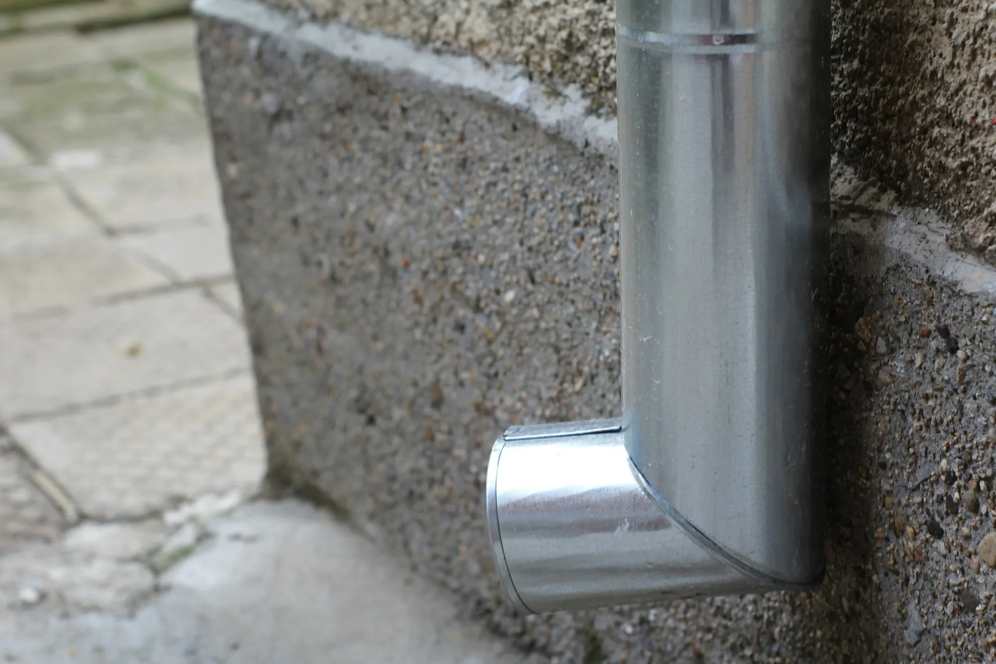 New metal downpipe outlet fitted against a render wall