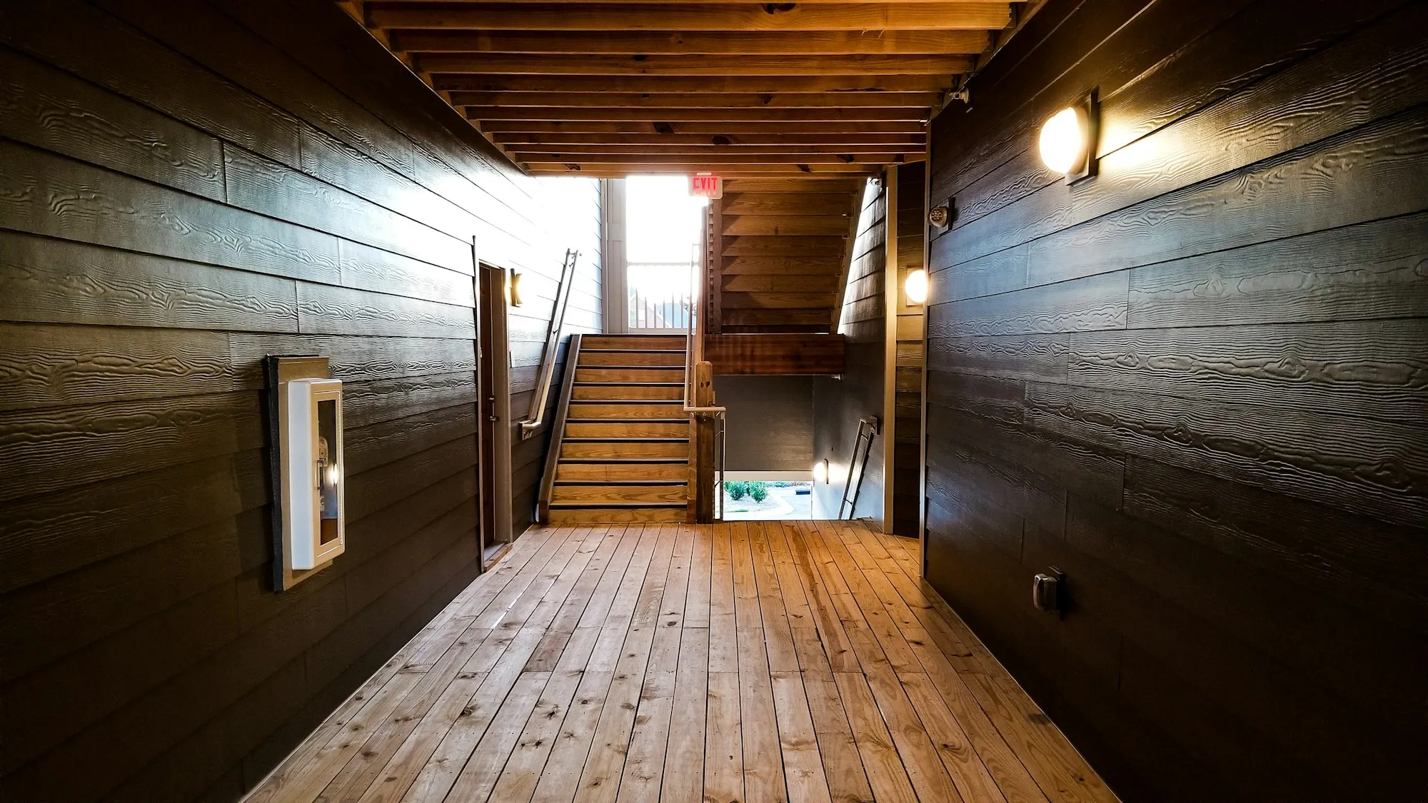 Timber-lined building corridor with wall lights and a stair at the end